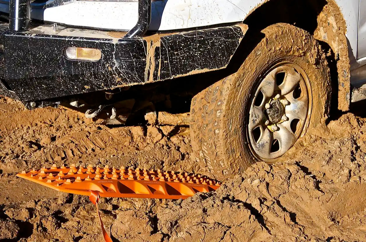 Brightly colored traction boards being placed under a vehicle's tires in deep mud.