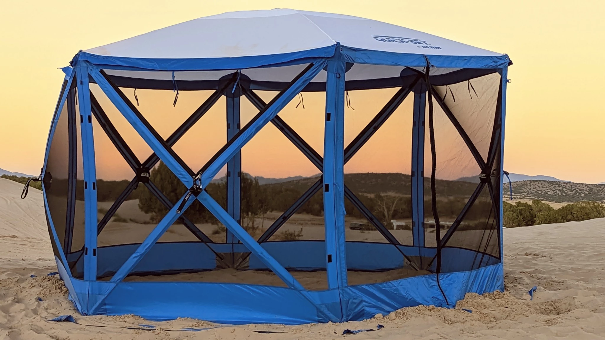 A fully enclosed green mesh screen house canopy set up in a wooded campsite providing insect protection.