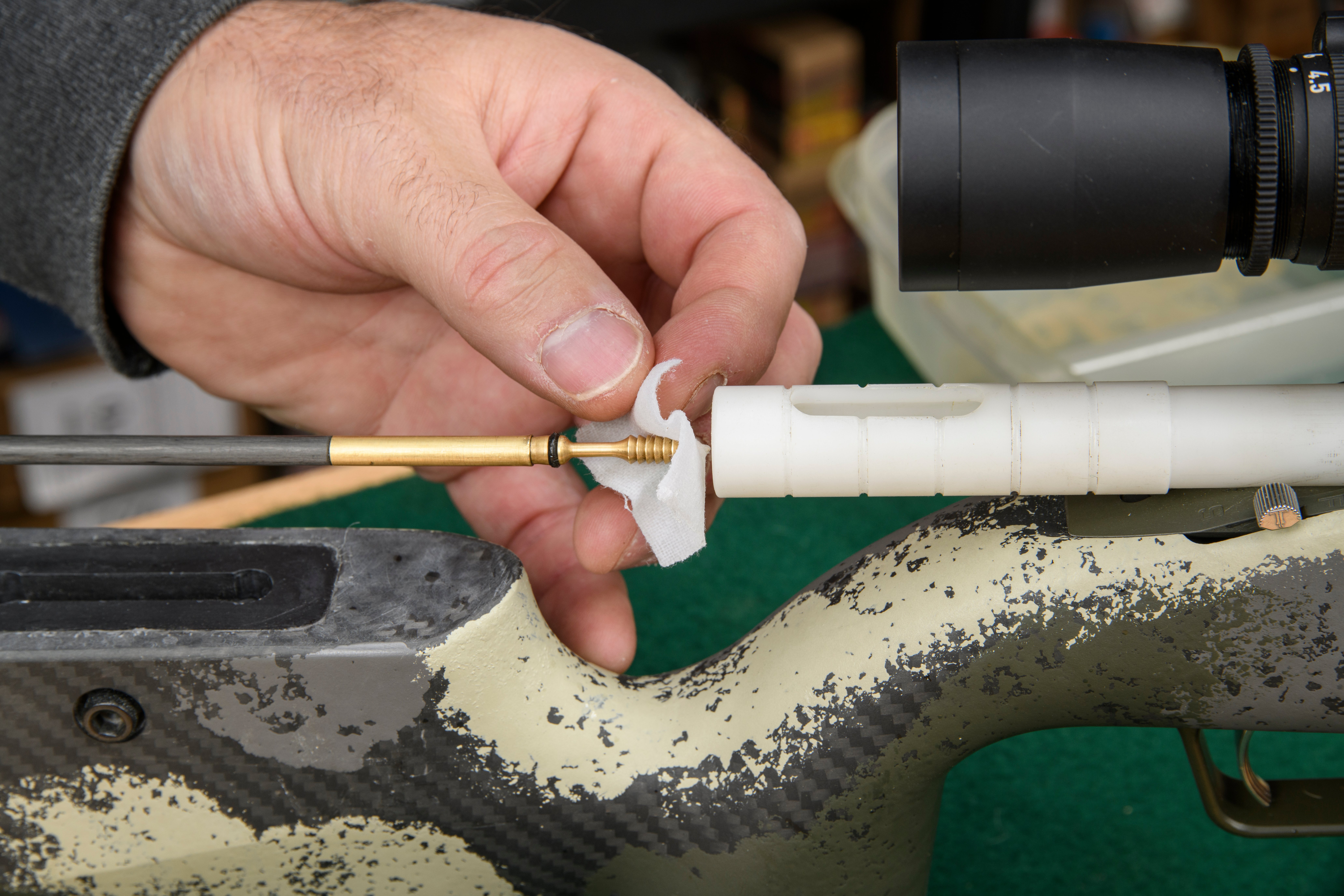 Someone placing a white cotton patch onto a brass cleaning jag attached to a rifle cleaning rod.