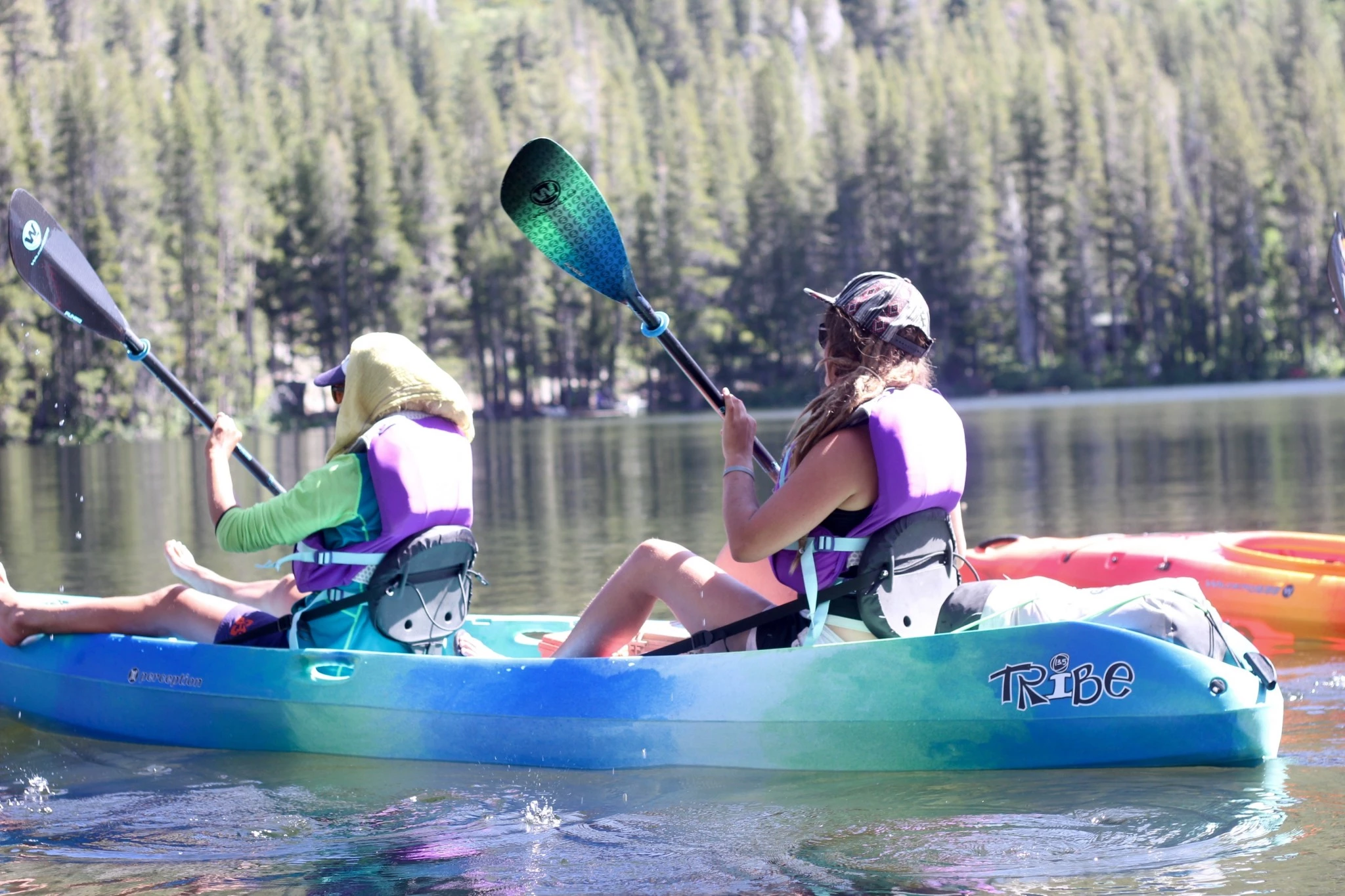 A blue Perception Tribe sit-on-top kayak being paddled on flat water.