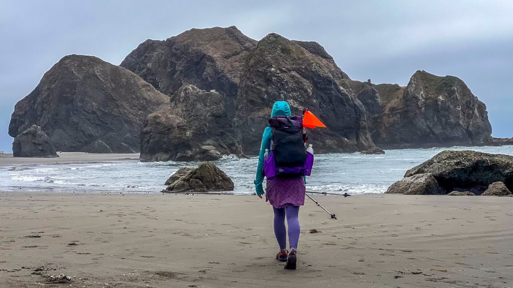 A lone hiker walking toward massive sea stacks on a hazy beach.