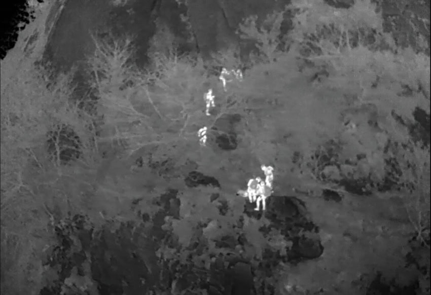 Thermal drone footage showing a glowing white human heat signature against a dark, cold background.