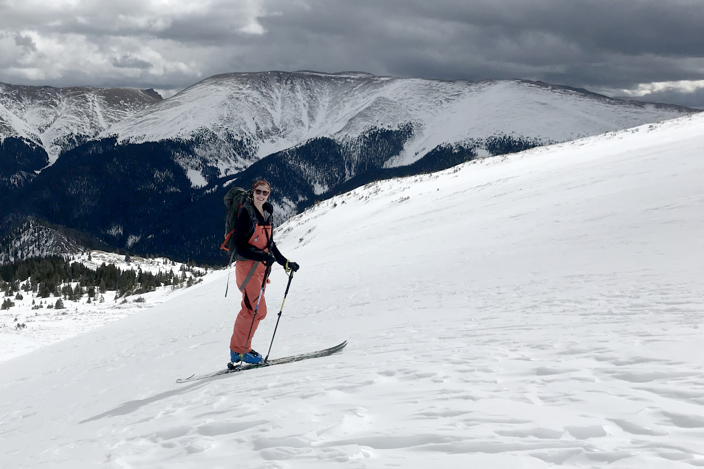Female skier wearing the pale pink Flylow Foxy Bib standing on a snowy mountain slope.