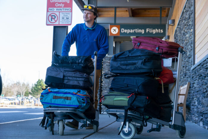 A tester navigating an airport with a luggage cart full of different backpack models.