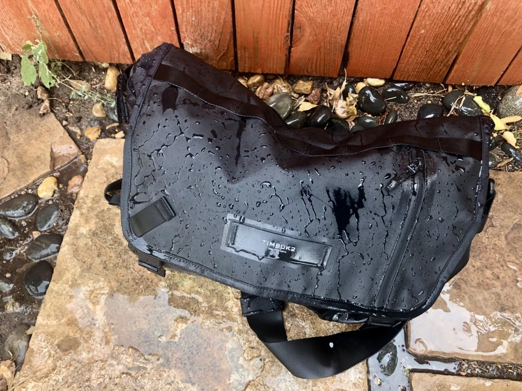 Close-up of water droplets beading and sliding off the fabric of the Especial Stash messenger bag.