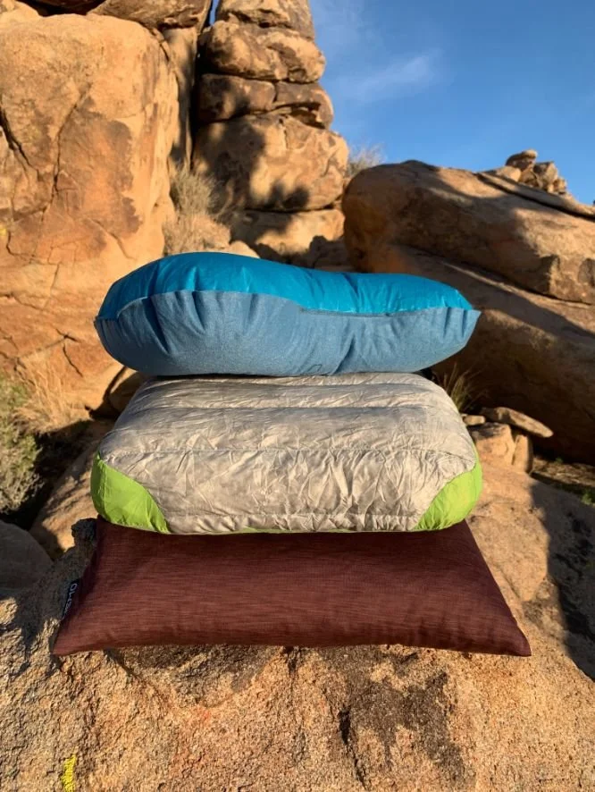 A vertical stack of three different types of backpacking pillows: inflatable on top, hybrid in the middle, and foam on the bottom.