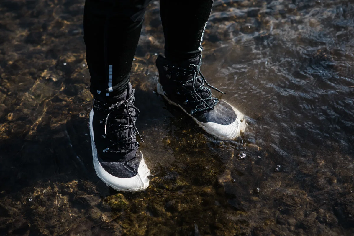 Close-up of Vivobarefoot boots stepping through water and mud on a trail.