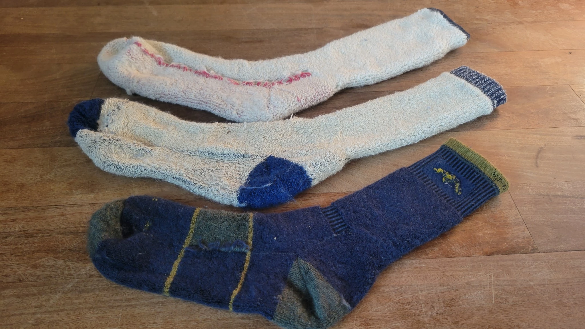 A stack of three different hiking socks showing the profile thickness of Smartwool, REI, and Darn Tough models.