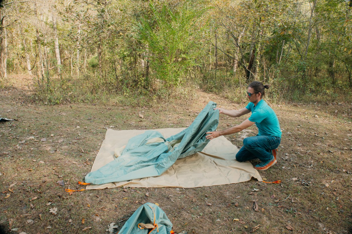 A camper assembling the tent poles in a wooded campsite area