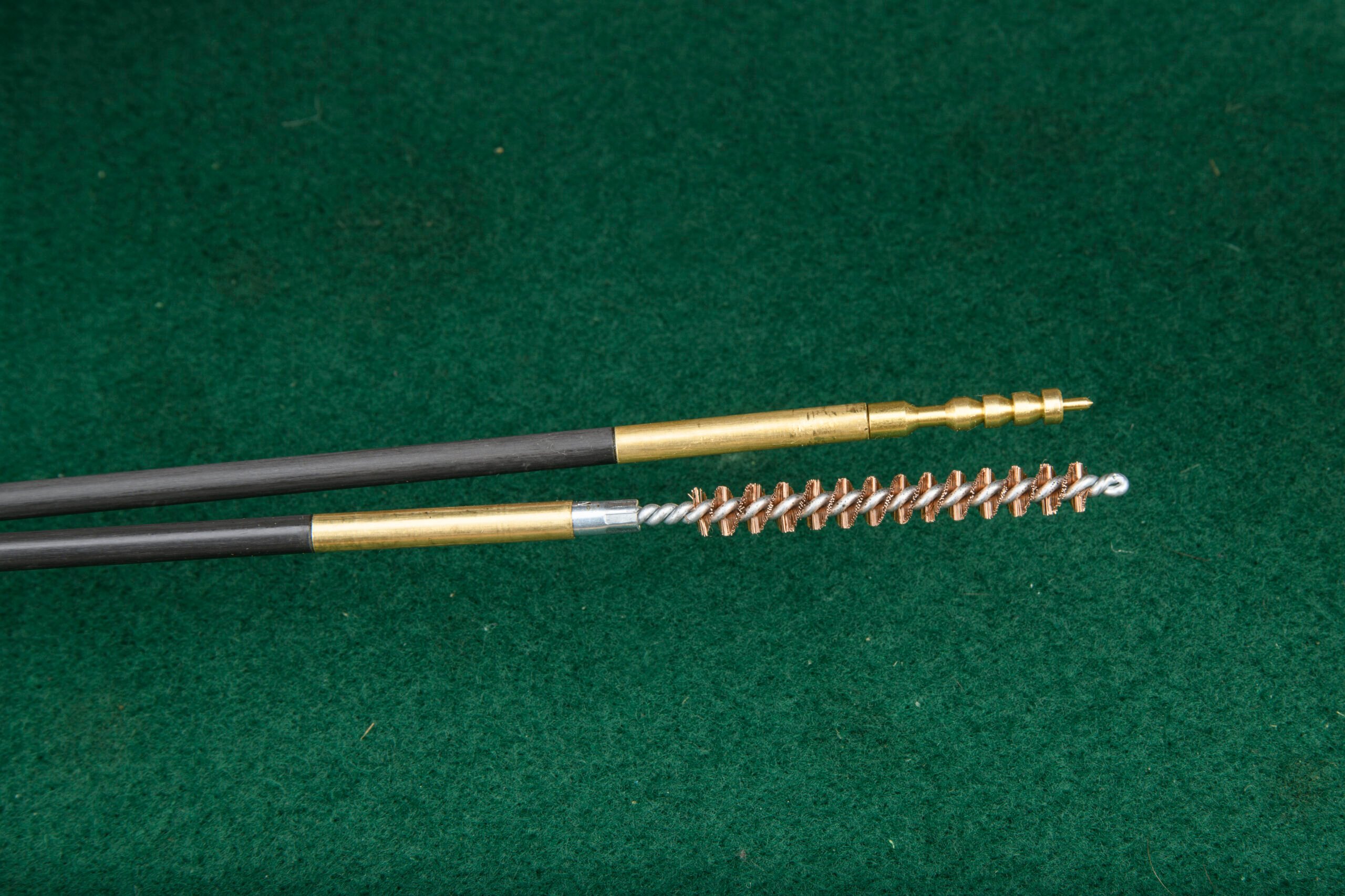 A collection of bronze bore brushes and cleaning jags on a green felt mat.