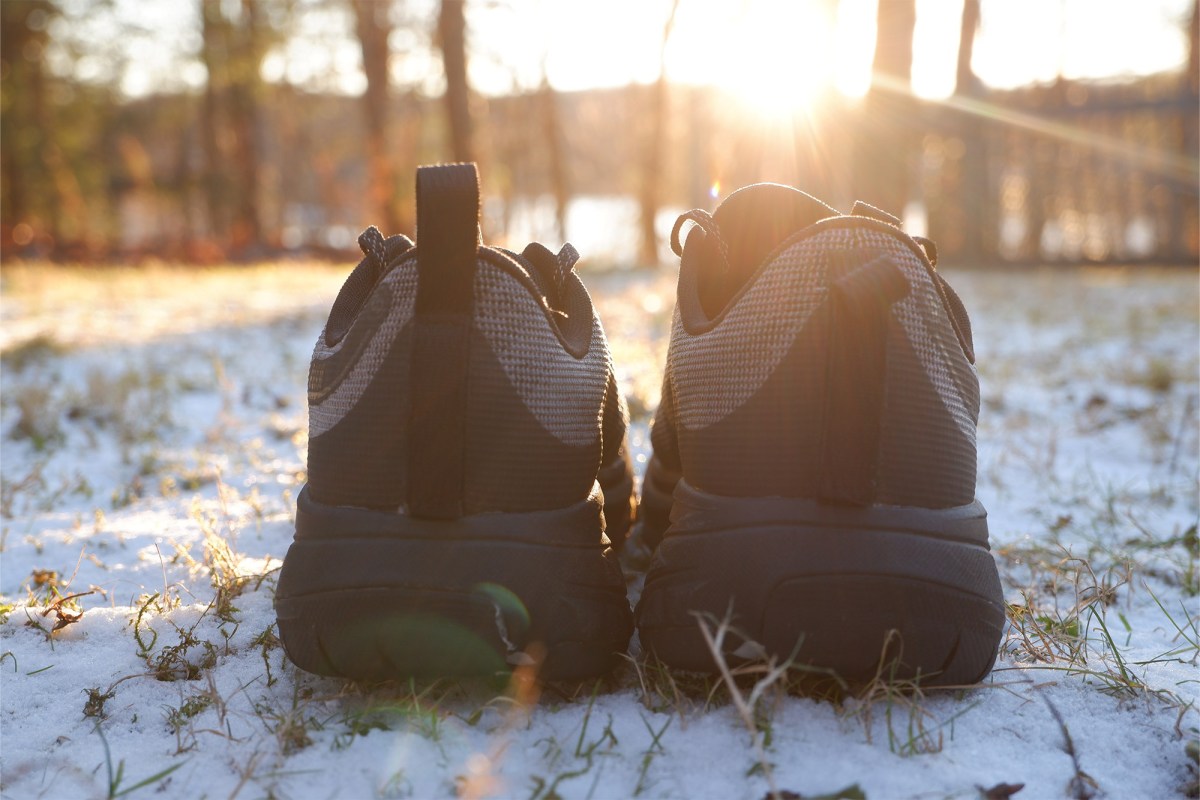 Rear view of KEEN Roam shoes sitting on snow with a soft mountain sun behind them.
