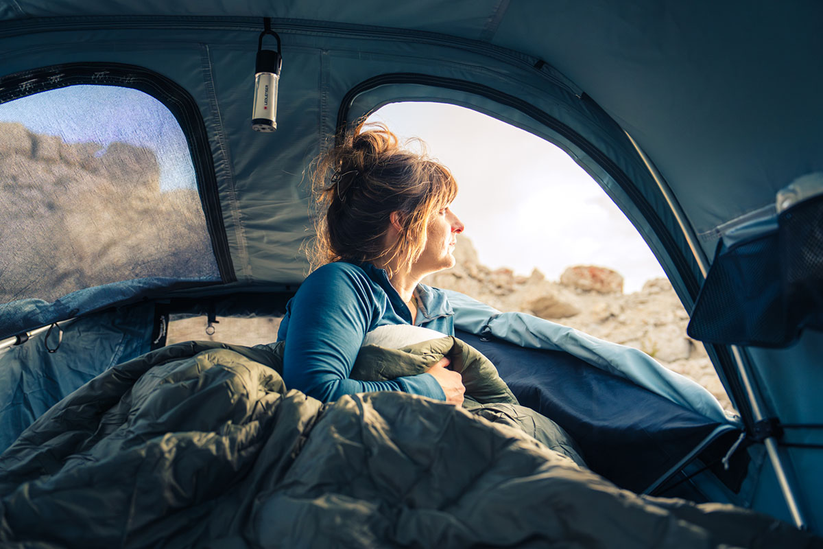 A sleeping bag laid out inside a rooftop tent with a scenic mountain backdrop.