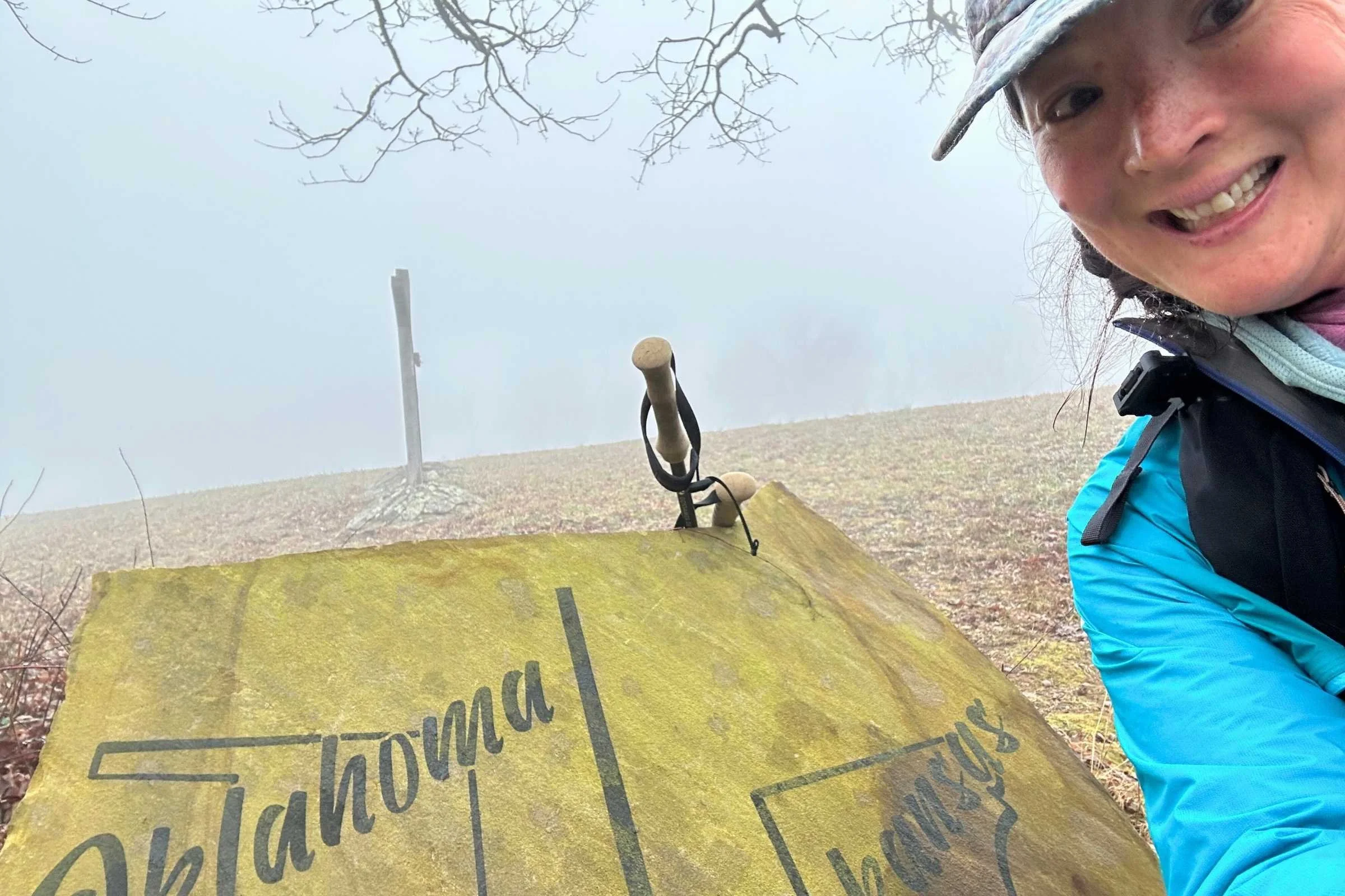 A hiker standing by the Oklahoma-Arkansas state line marker on the Ouachita Trail.
