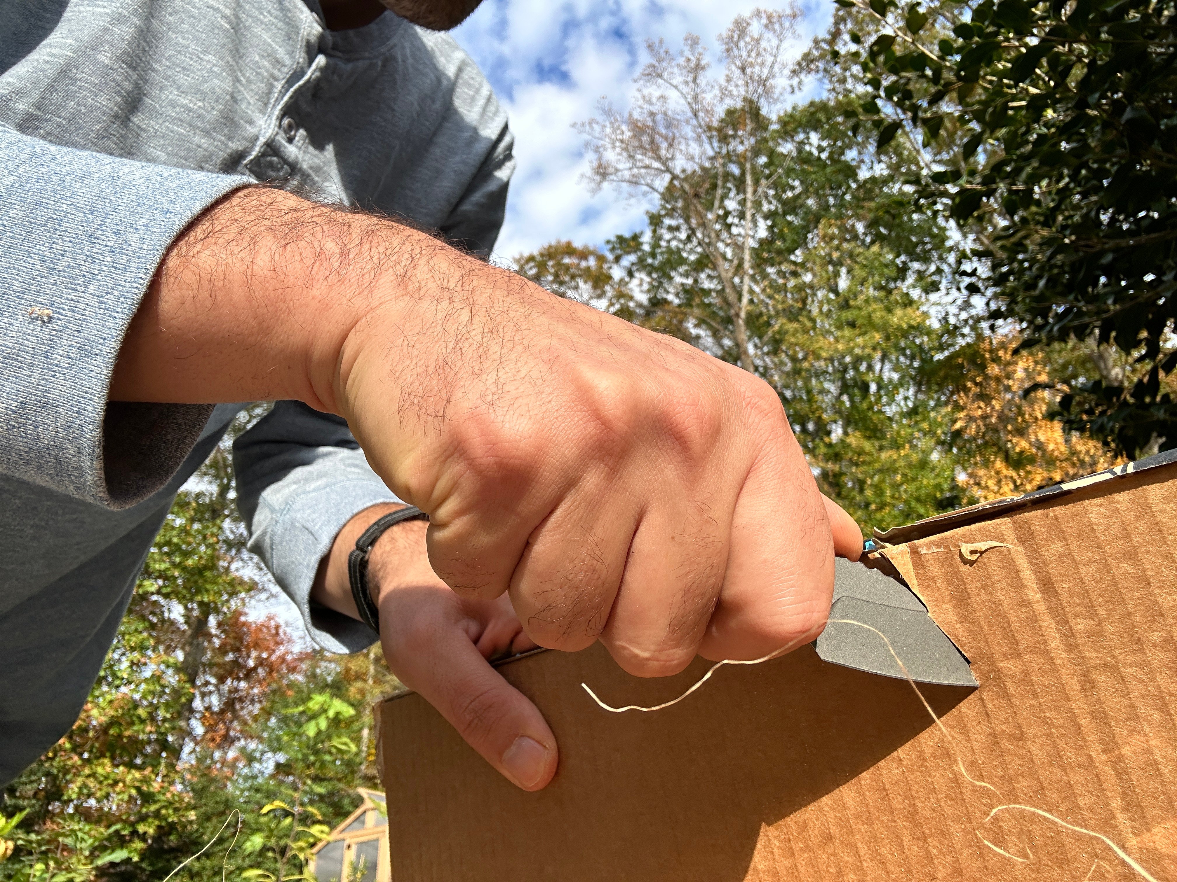 A person using a folding knife to slice a piece of wood to test edge sharpness.