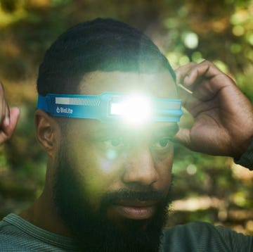 A man running through a dark forest with a powerful headlamp beam illuminating the trail ahead.