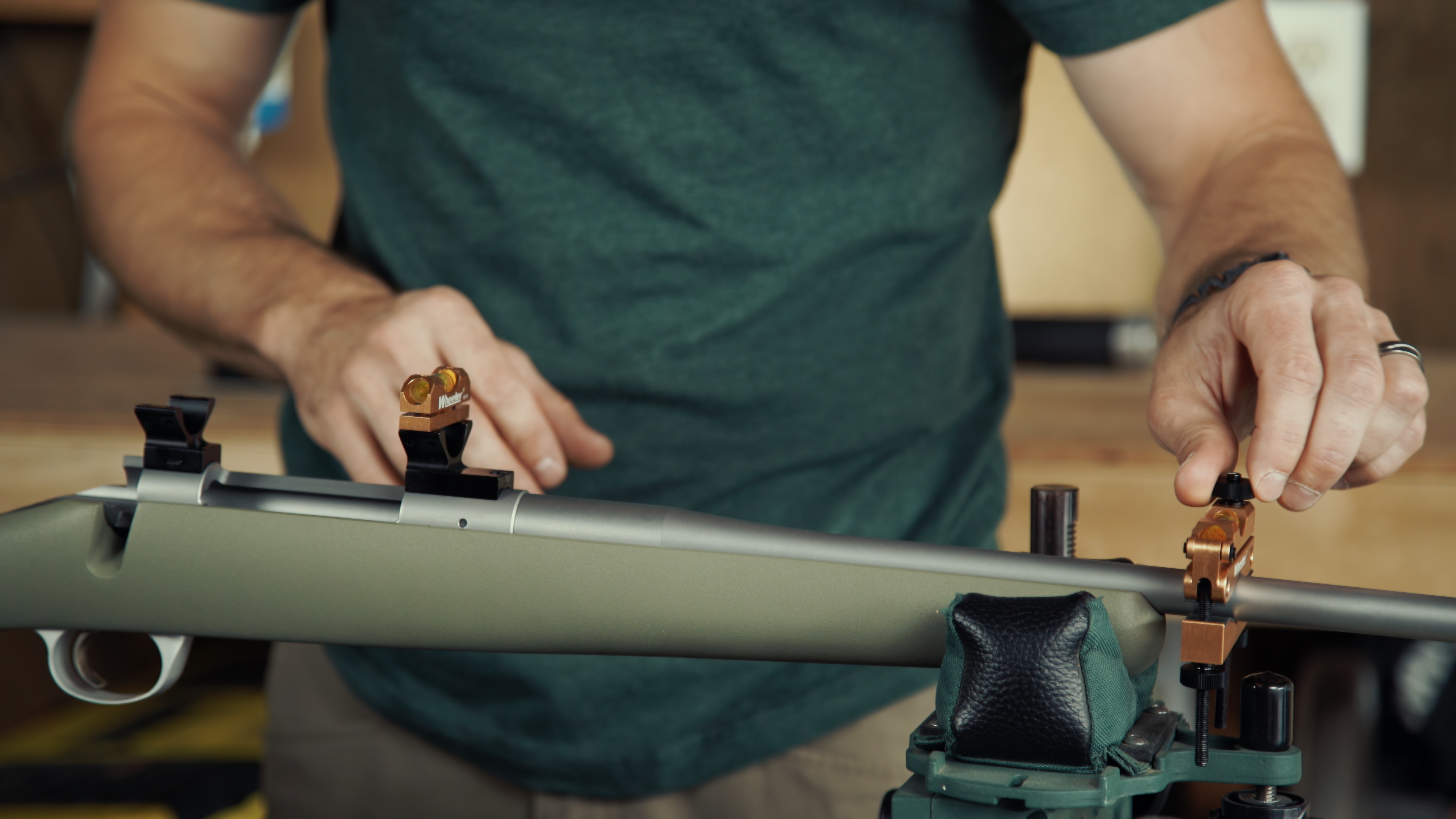 Close-up of hands adjusting the scope rings on a rifle to ensure even spacing and alignment.