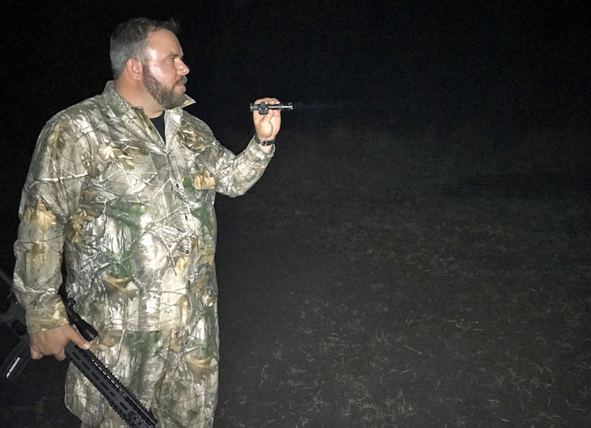 A hunter carefully stalking a sounder of hogs across an open field at night.