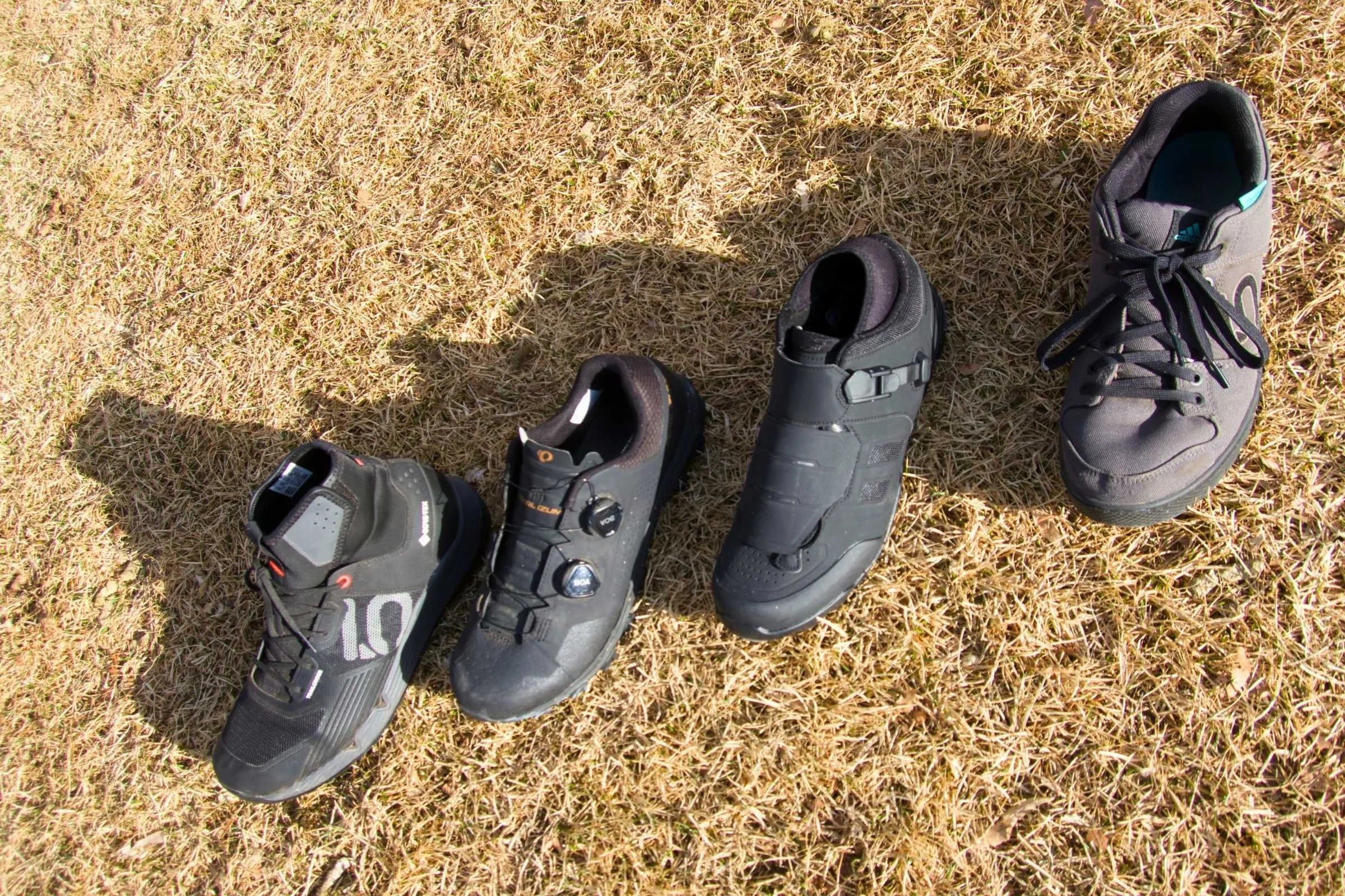 A group of tested mountain bike shoes lined up on a wooden surface, including Five Ten and Shimano models.