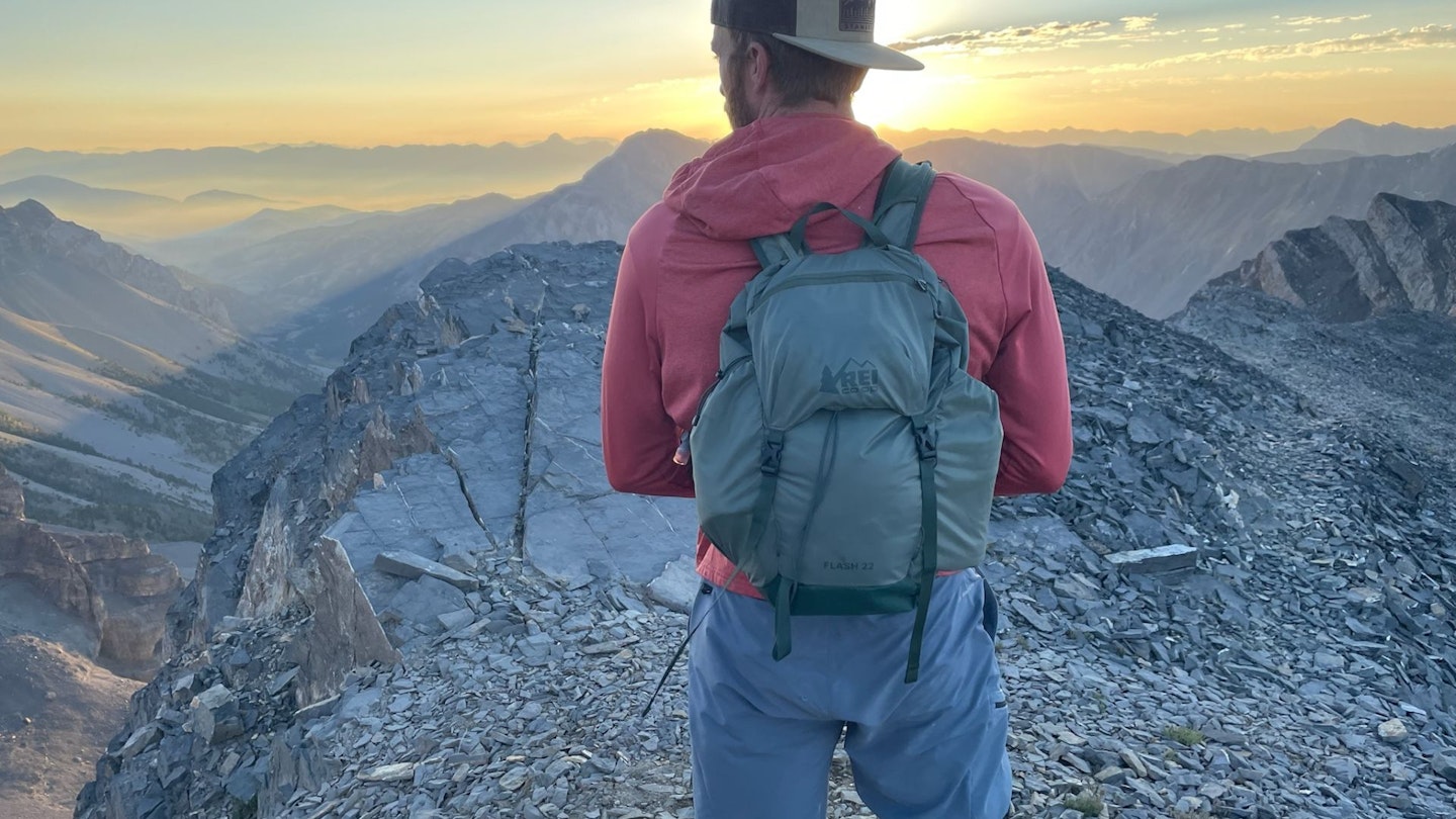 A hiker wearing a compact blue REI Co-op Flash 22 pack on a rocky trail.