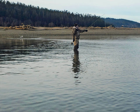 An angler fully equipped with chest waders and a fly fishing vest wading in a clear river.