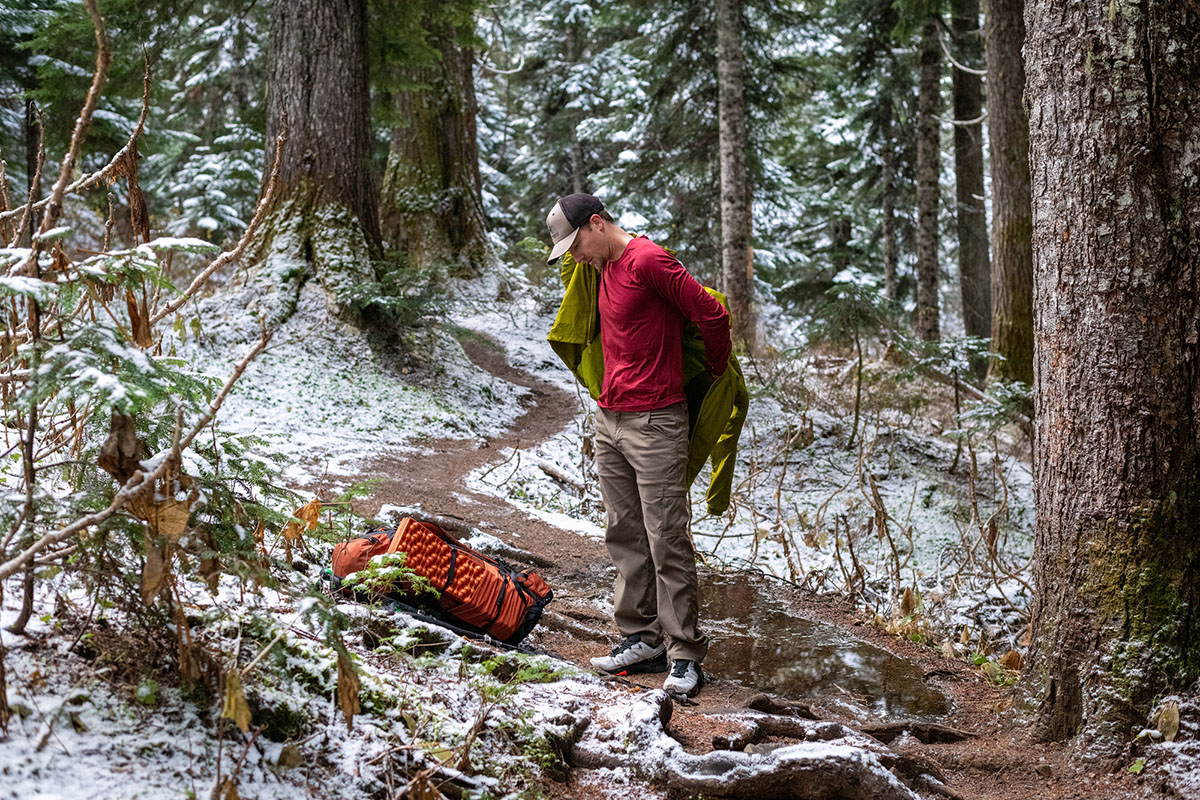 A man putting on a technical jacket over a base layer.