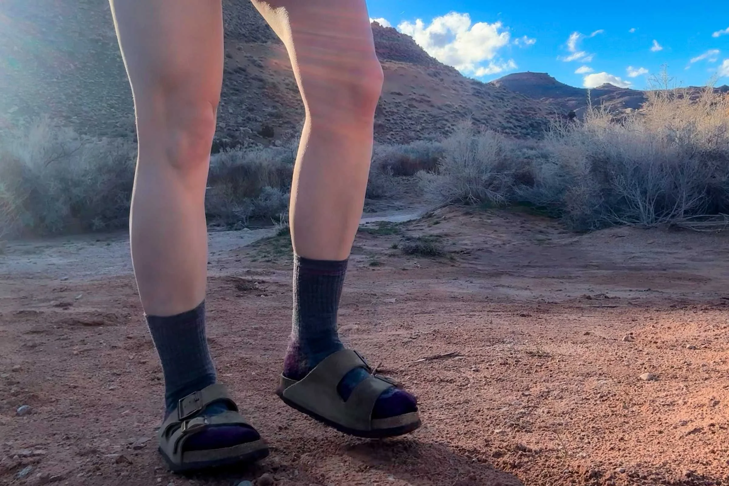 A person wearing classic Birkenstock Arizona sandals while standing on a desert trail.