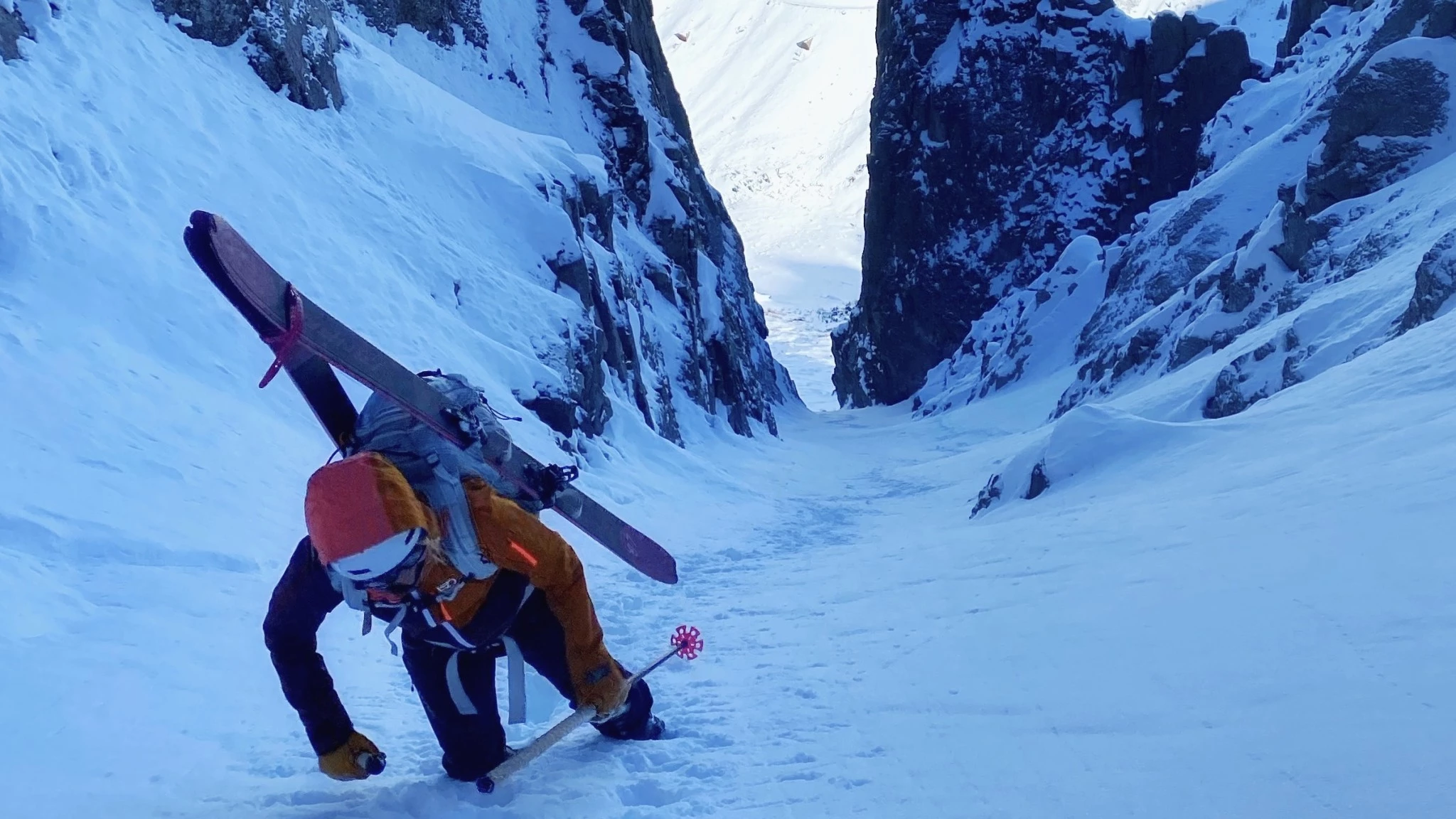 A woman wearing an Ortovox Ortler 3L hardshell jacket while skinning uphill in a snowy mountain environment.