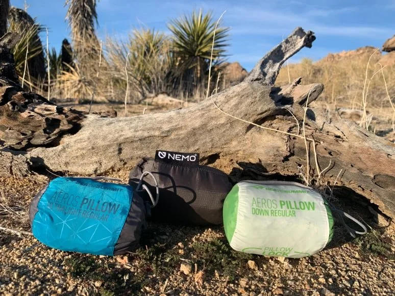 Comparison of three backpacking pillows packed into their small stuff sacks next to a hand for scale.
