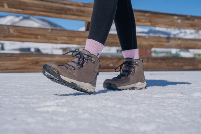 A woman walking over a snow-dusted wooden bridge in winter boots.