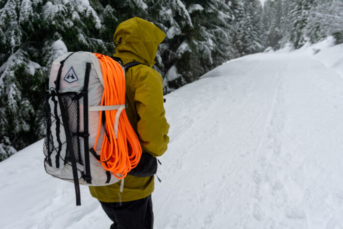 A person wearing a blue Arc'teryx jacket and a heavy backpack looking out over a mountain range.