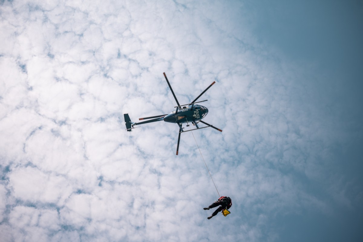A search and rescue helicopter performing an airlift operation over rugged mountain terrain.