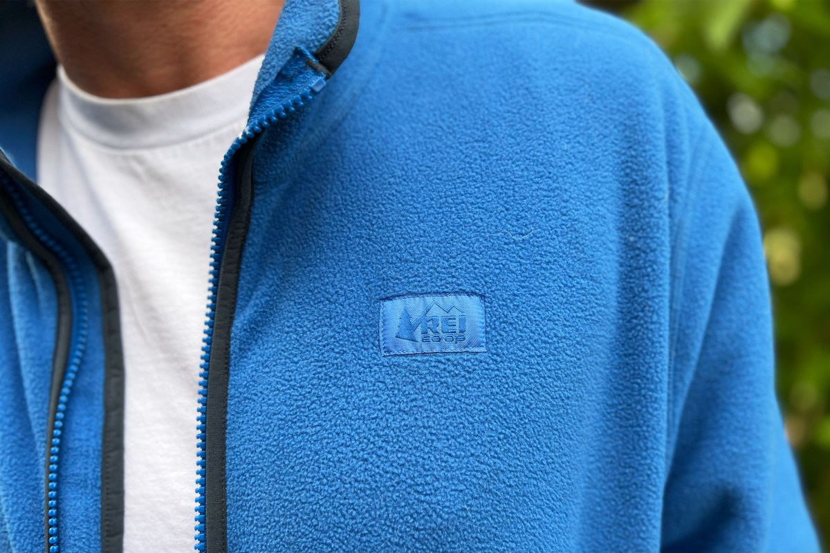 A hiker wearing the REI Trailmade Fleece Jacket standing on a forested trail.